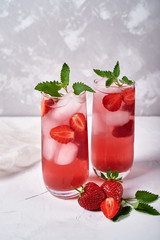 Fresh strawberry lemonade with ice and mint in glass on table, copy space. Cold summer drink. Sparkling glasses with berry cocktail