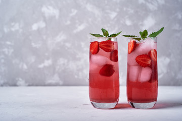 Fresh strawberry lemonade with ice and mint in glass on table, copy space. Cold summer drink. Sparkling glasses with berry cocktail