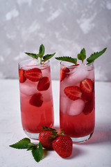 Fresh strawberry lemonade with ice and mint in glass on table, copy space. Cold summer drink. Sparkling glasses with berry cocktail