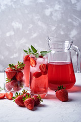 Fresh strawberry lemonade with ice and mint in glasses and jug on white table background, copy space. Cold summer drink. Sparkling glass with berry cocktail