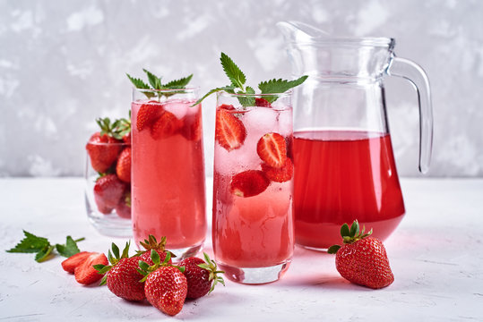 Fresh strawberry lemonade with ice and mint in glasses and jug on white table background, copy space. Cold summer drink. Sparkling glass with berry cocktail