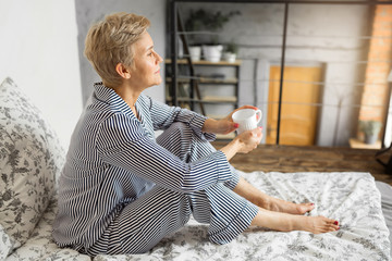 adult elderly woman in pajamas in bed in the bedroom with a mug