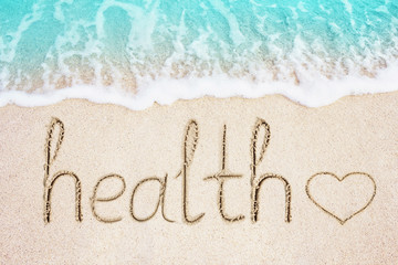Fototapeta na wymiar Health text and heart symbol written in sand. Ocean blue wave on background. Healthcare and wellness concept photo.