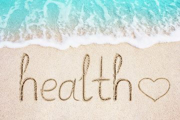 Health text and heart symbol written in sand. Ocean blue wave on background. Healthcare and...