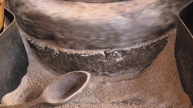 Close-up footage a process of grinding grain on an old millstone of medieval hand-driven millstone grinding wheat. The ancient Quern stone hand mill with grain. A miller grinds the grain into flour