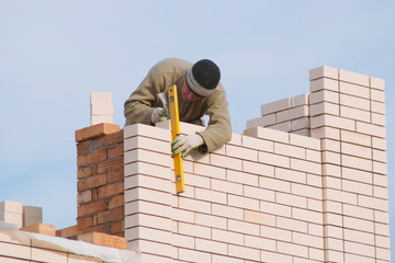 Fototapeta premium A bricklayer puts a facing brick. A bricklayer works on building a house - he puts a white facing brick