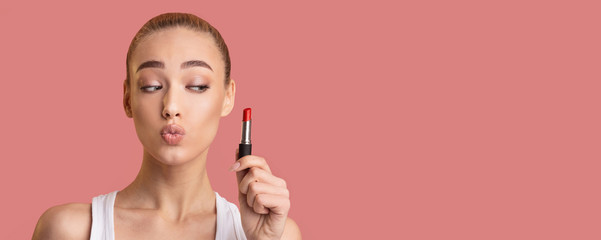Young Woman Holding Lipstick Standing On Pink Background In Studio