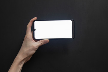 Phone with a bright screen in a horizontal position holds his hand against a dark background.