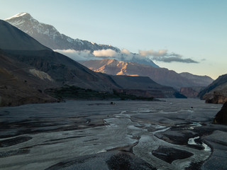 The wide river bed of the Kali Gandaki valley surrounded by the barren snow covered Himalayan mountains of the cold desert landscape of Upper Mustang on the Annapurna Circuit trail in Nepal.