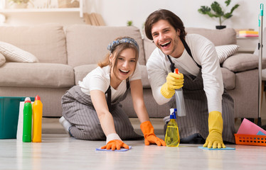 Young happy couple in rubber gloves cleaning floor in their apartment