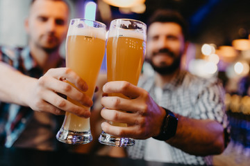 Happy two men friends clinking with beer mugs in pub