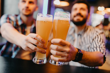 Close up Friends toasting with glasses of light beer at the pub. A group of young people while relaxing at the bar.