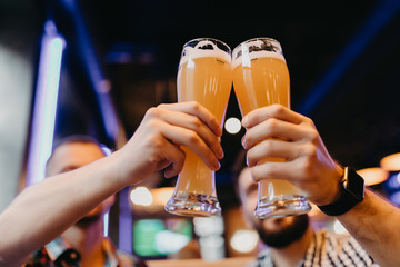 Close up Friends toasting with glasses of light beer at the pub. A group of young people while relaxing at the bar.