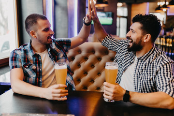 Handsome cheerful friends giving high five while drink beer in pub