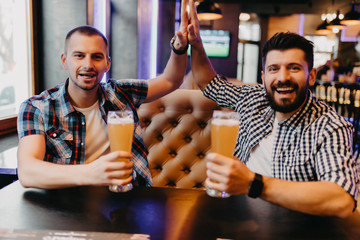 Handsome cheerful friends giving high five while drink beer in pub