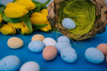 Happy Easter. Easter holiday decorations on trendy colored classic blue background. Creative spring composition with Easter elements - flowers and eggs in basket. Celebrating Easter concept at spring.
