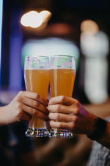 Close up of hands of two friends toasting with glasses of light beer at the pub.