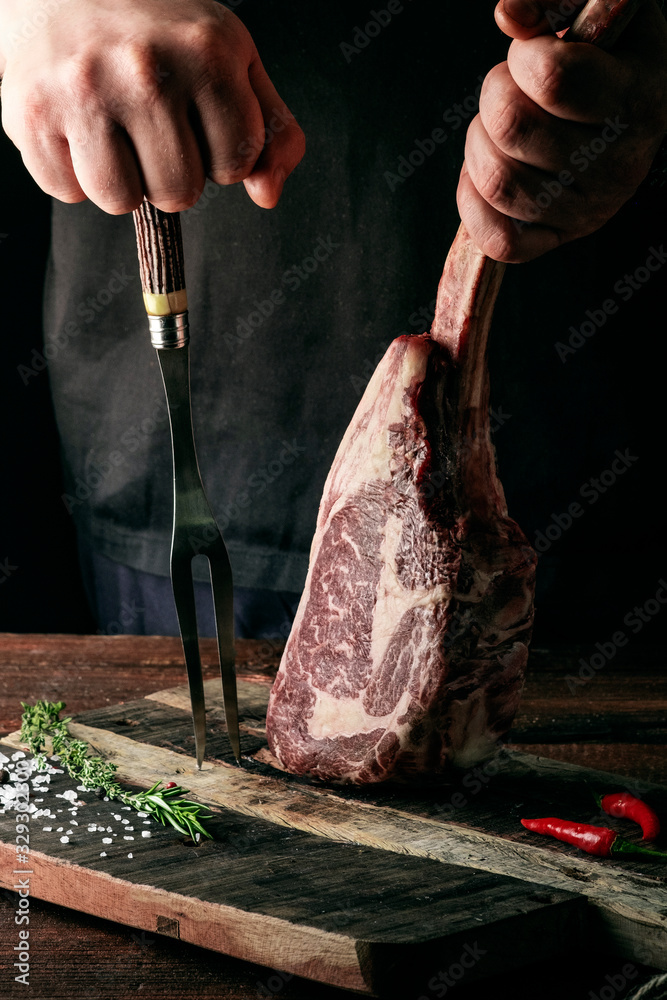 Wall mural a man holds a raw tomahawk steak on a bone of dry aged beef on a dark background