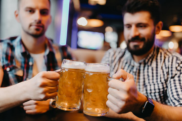 Handsome friends are clinking glasses of beer and smiling while resting at the pub