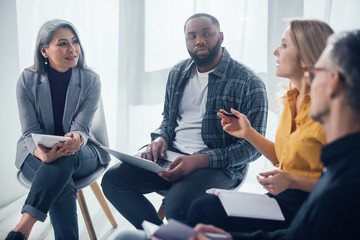 selective focus of multicultural colleagues with gadgets sitting and talking in office