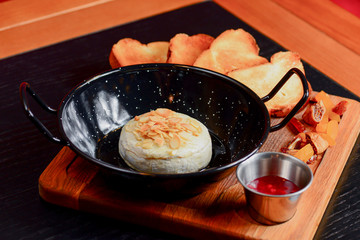 Baked Cheese - Melted cheese with bread and sauce served in a bowl on wooden rustic cutting board.