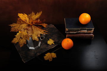 High angle shot of two oranges and old vintage book with a pewter carafe on top.  Fading maple...