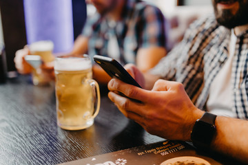 Close up of Young men friends with smartphones drinking beer at pub