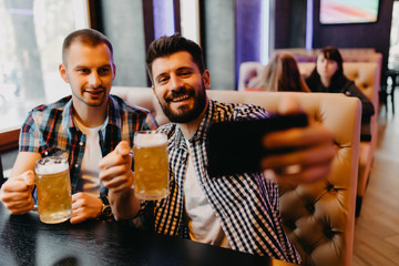 Happy male friends with smartphone taking selfie and drinking beer at pub
