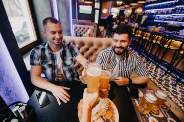 Old friends meeting. Three cheerful young men drinking beer in pub