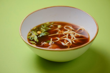 Asian style beef noodles soup served in white bowl over bright green background.
