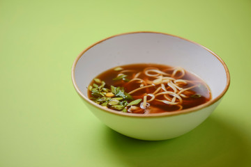 Asian style beef noodles soup served in white bowl over bright green background.
