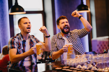 Happy two men shouting while watching football match broadcast in pub