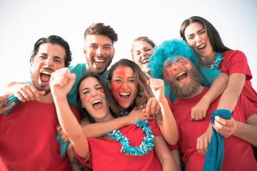 Obraz premium Football fan screaming, with red shirts inside of the stadium . Group of young people very excited about football. Sport and fun concept - Image
