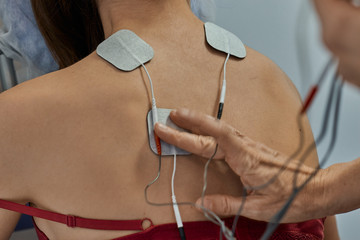 Electro stimulation in physical therapy to a young woman. Medical check at the shoulder in a...