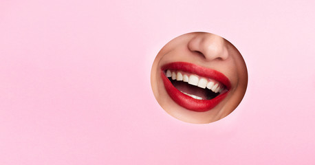 Woman showing red lips out of pink paper hole