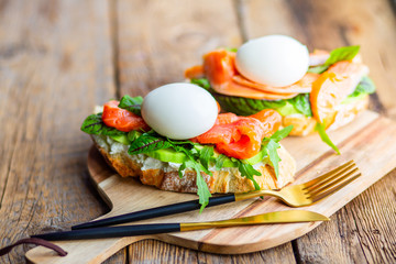 Toast with poached egg, avocado, arugula, cheese, red fish with herbs. Tasty lunch. Proper nutrition with healthy fats. Delicious toast with avocado. Eggs of Benidict. Poached egg spreads on toast