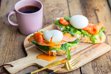 Toast with poached egg, avocado, arugula, cheese, red fish with herbs. Tasty lunch. Proper nutrition with healthy fats. Delicious toast with avocado. Eggs of Benidict. Poached egg spreads on toast