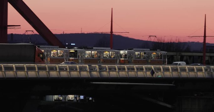 BUDAPEST, HUNGARY - CIRCA 2020: Tram line 1 crossing the river Danube to Lagymanyos on the Rakoczi Bridge, after sunset twilight glow, cars passing by