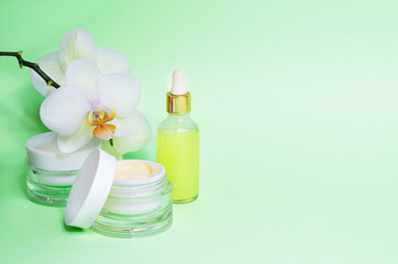 natural cosmetic product for facial. cream, mask, serum with vitamin C, orchid on green background. copy space. beauty concept