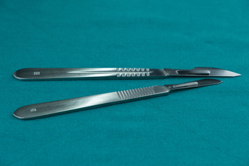 Surgical instrument, stainless steel scalpel handle number 3 with blade number 10 and scalpel handle number 4 with blade number 24 on surgical green drape fabric.