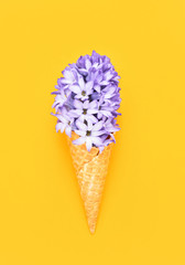 Waffle ice cream cone with purple hyacinth flower on yellow background. Spring concept. Copy space, top view