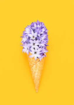 Waffle ice cream cone with purple hyacinth flower on yellow background. Spring concept. Copy space, top view