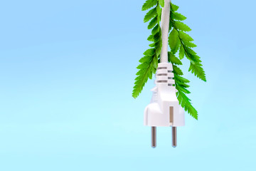 Electric white plug with green leaves hanging  and isolated on blue background. Eco friendly, alternative ecological energy,  ecology concept. Copy space.