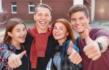 Happy smiling group of students giving thumbs up near university on background