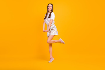 Full size profile photo of funny lady walking down street enjoy sunny day flirty mood wear casual white t-shirt striped shorts shoes isolated vibrant yellow color background