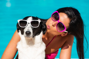 Happy woman and cute dog wearing sunglasses and having fun on summer vacation at swimming pool.