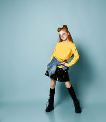 Cool red-haired teen girl in yellow sweatshirt, black skirt, stockings and brutal shoes is posing like a top model