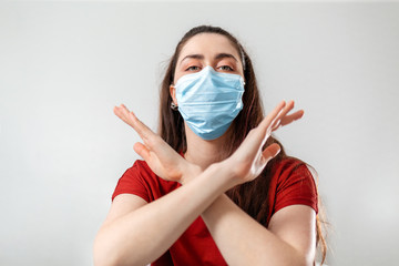 A woman in a red t-shirt and medical mask crosses her arms in front of her, on a white background. Bottom view. Philosophy of health, medicine and protection from viral infection