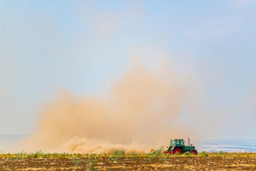 Ein Traktor pflügt ein trockenes Feld an einem heißen Tag.