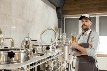Professional brewer on his own craft alcohol production. Specialist, man wearing in workwear testing, trying product on its taste, color and smell. Concept of open business, eco product, craft brewery